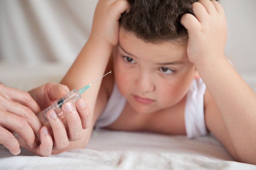 scared little overweight boy grabbed his head frightened by the hand of doctor with vaccine